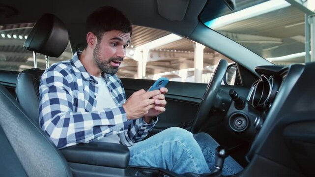 Smiling guy looking at phone screen while sitting in the car. Slow motion