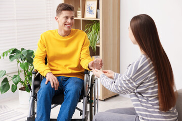 Fototapeta premium Woman giving glass of water to man in wheelchair at home