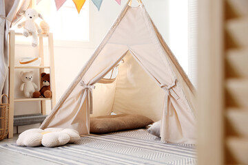 Stylish toy wigwam, pillows and decor in light playroom. Interior design © New Africa
