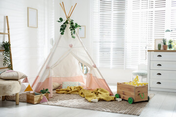 Toy wigwam with pillows, wooden cart, furniture and floral decor in room © New Africa