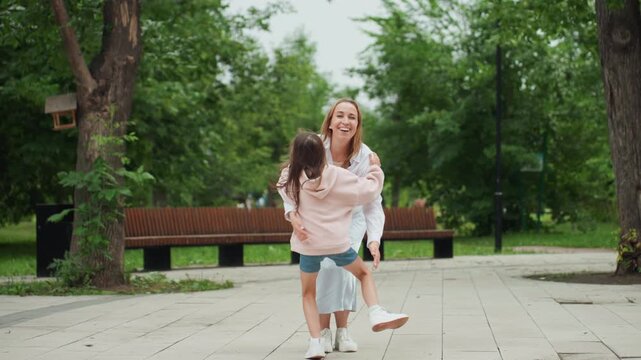 Child hugs mother. Girl embraces caring mother outdoors. Young girl is embraced by her protective mother in park. Child is gently held by mother amidst leafy park surroundings during tender moment