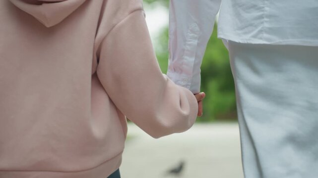 Mother and daughter stroll through park. Parent and young girl walk hand in hand peacefully. Mother and her daughter meander along shaded park pathway peacefully enjoying warm summer light