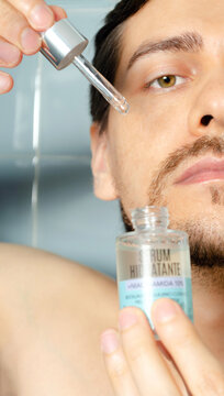 Hombre aplicando s&eacute;rum facial hidratante con gotero sobre mejilla durante rutina de skincare masculino