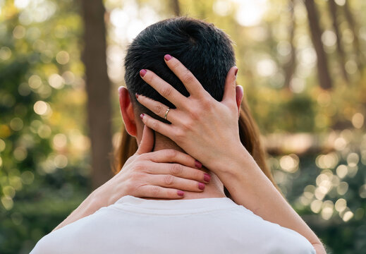 Detalle de manos de mujer abrazando la cabeza y el cuello de un hombre en un bosque; concepto de apoyo emocional, amor y cuidado.