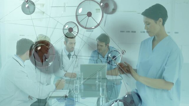 Medical team doing case review at laptop as nodes drifting over group spurring nurse tapping tablet
