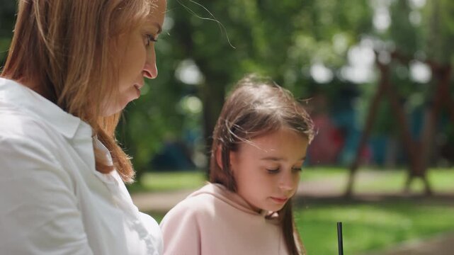 Mother and daughter sharing snack. Bright outdoor setting capturing mother and daughter passing treat. Tranquil scene of family love beneath sunlit trees with shared treats and smiles