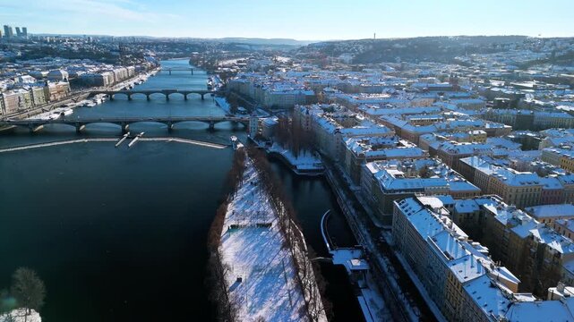 Aerial view of snowy Prague, Czech Republic. Winter cityscape with Snow-covered rooftops, Vltava River, and sunny blue sky