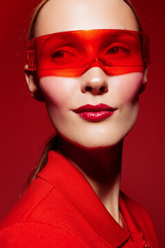 Portrait of confident woman wearing red transparent visor and red outfit against red background. Fashion concept with bold makeup and futuristic style in studio lighting.