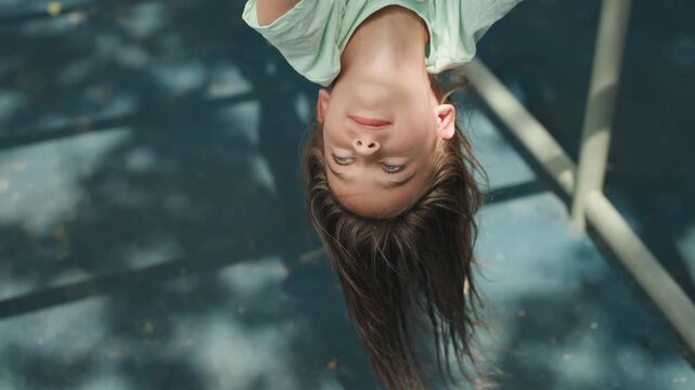 Daughter inverted closeup portrait under trees, braided hair hanging down and soft sunlight dappled across face, calm gaze and gentle expression, childhood wonder and quiet play, serene summer mood