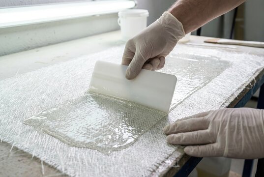 Worker wearing gloves using a plastic squeegee to spread clear epoxy resin over fiberglass cloth