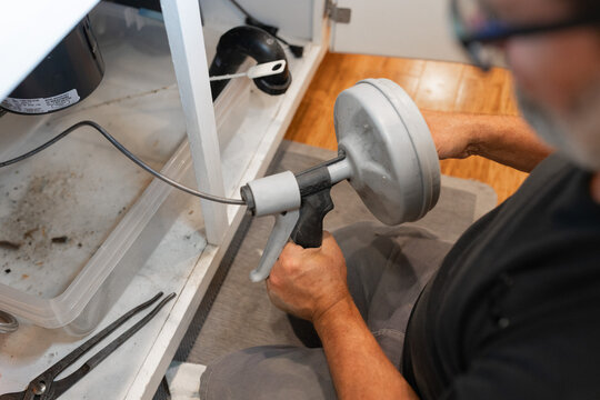 A plumber uses a drain snake, or auger, to clear a blockage from a pipe, water supply, installations, garbage disposal repair, drain cleaning
