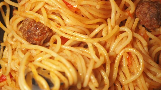 Cinematic close up of fork twisting through spaghetti with tomato sauce and meatballs in a slow motion footage.