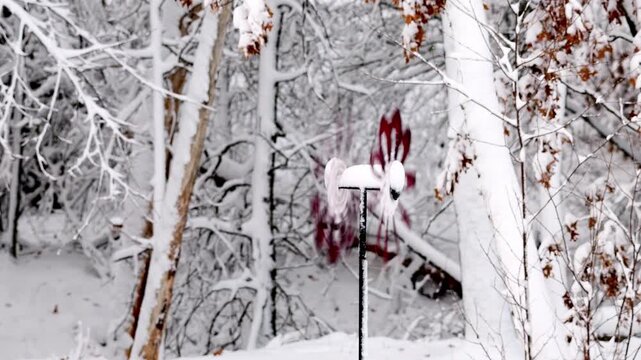 A red wind spinner, covered with snow, spins in opposing directions and rotates as the wind blows outdoors in a winter back yard scene after a snowfall. Bidirectional spinning.