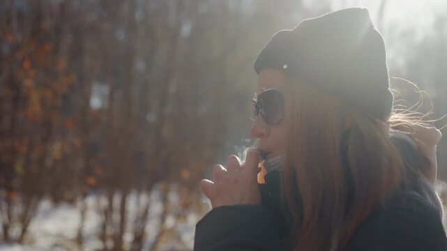 White woman profile in snowy woodland inhaling cigarette, red hair tucked under beanie and sunglasses backlit vapor and cold breath, contemplative solitude with subtle thief implication, cinematic