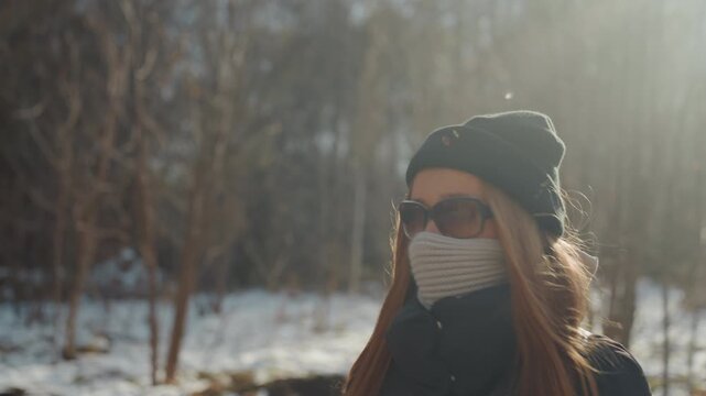 Woman walking outdoors. Snowy trail with backpack woman. Silhouetted woman on winter trail with hat. Rural winter scene showing woman with backpack and beanie cautiously walking trail