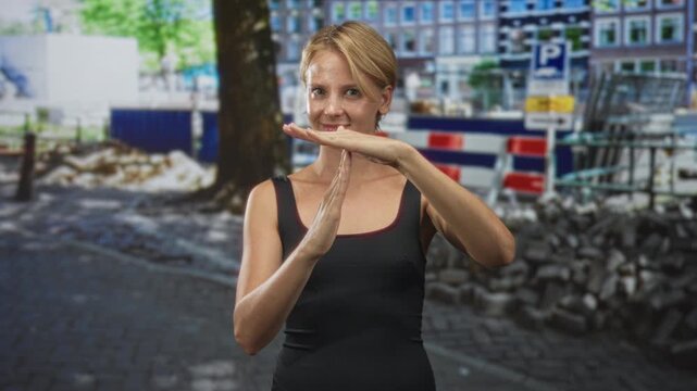 Woman shows timeout with hands in street construction area by barrier and cobblestones wearing black tanktop; confidence calm.
