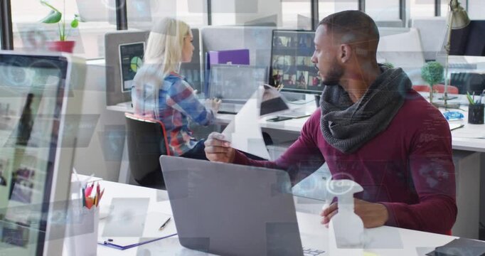 Handing man wearing maroon sweater scarf passing paper to coworker in plaid shirt, office, laptop
