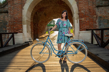 Obraz premium Young beautiful woman on spring day, posing with her bicycle , standing on wooden bridge at sunset 