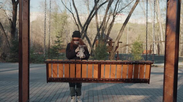 Park planter swing wooden bench snatcher steps into center, pauses to inspect planter edge, conceals movement with jacket, quickly snatches object and moves away, candid street footage, autumn light,