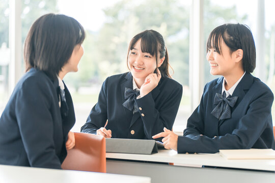 Elementary, middle, and high school students (including female high school students who are friends) talking to the student sitting in front of them during class.