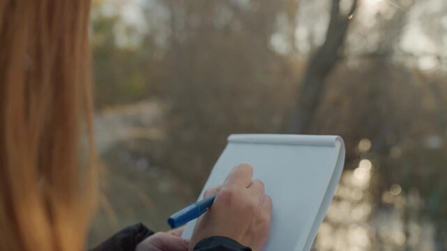 Woman notes outdoors. Caucasian woman documenting details during field study along riverbank. Female scientist making careful notes while exploring scenic trail by shimmering water source