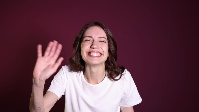 Happy woman waving hello on burgundy background