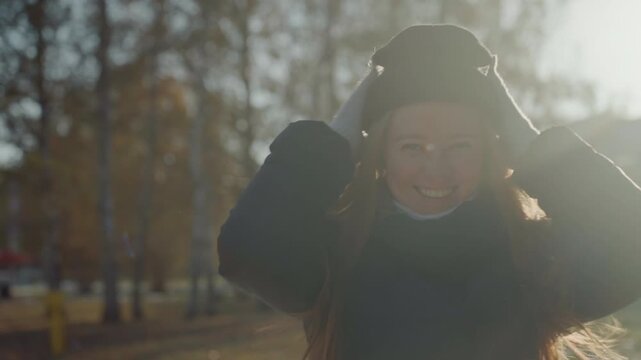 Backlit autumn park portrait white woman radiant smile windtousled hair, redhaired caucasian student adjusts beanie and scarf, golden rimlight, candid laughter, chilly atmosphere, intimate closeup,