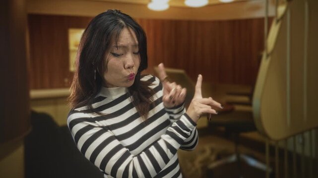 Woman with palms outward hand gesture and pursed lips in a building booth, wearing striped sweater and visible ring as she pushes away with fingers; disapproval dismissal.