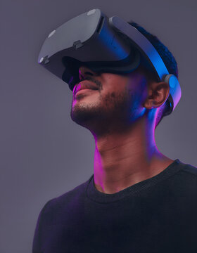 Asian man using a virtual reality headset in a modern studio with neon reflections, representing immersive technology, innovation, and future digital experiences.
