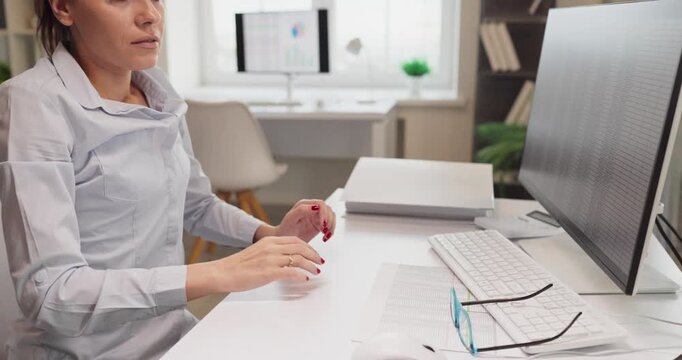 Tired woman businesswoman at computer in office. She massages her temples showing fatigue and stress from overwork, long screen time and tight deadlines. Clear concept of tired office worker.