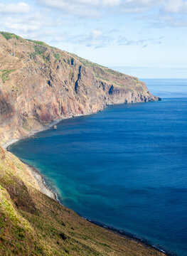 Ponta do Pargo cliffs. Steep rocky cliffs drop to a narrow shoreline. Deep blue Atlantic waters stretch along Madeira's western coast. View from Miradouro Farol da Ponta do Pargo in Portugal.