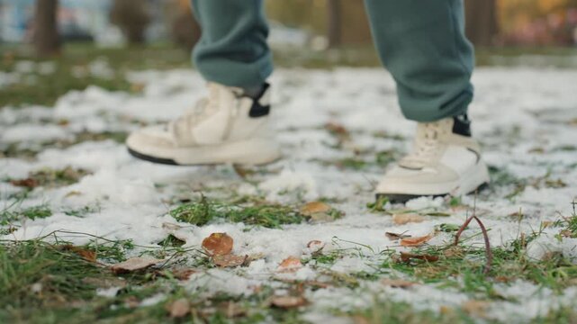 Closeup sneakers stepping on snow and grass, cautious prowler movement across melting patches and fallen leaves in urban park, tense quiet atmosphere, ankle and sole detail, hint of snatcher narrative