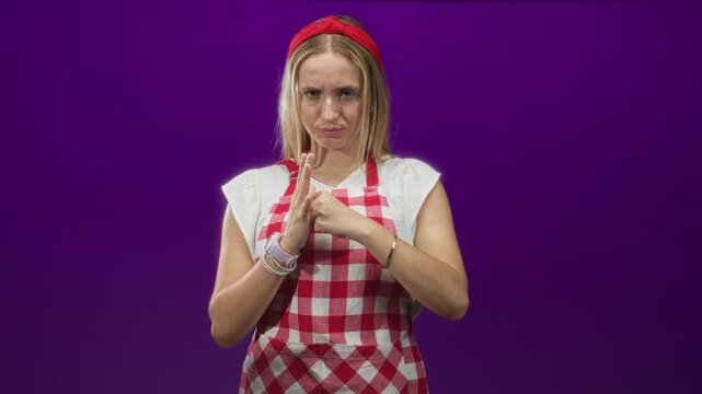 Woman in red check apron raises open hand and clenches other fist in studio; defensive stance frustration.