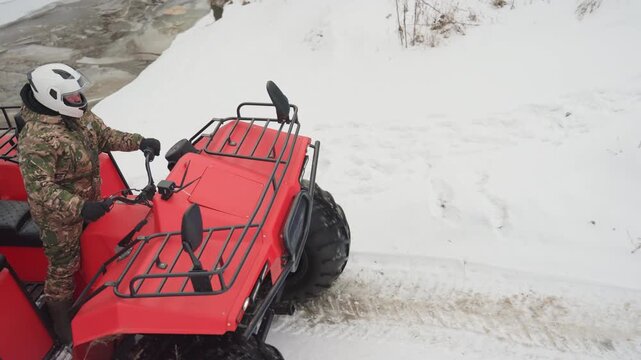 Red atv climbing snowy hill, rider powers up steep slope with throttle and traction control, tires digging into frost and loose snow, skid marks and spray create dynamic offroad scene