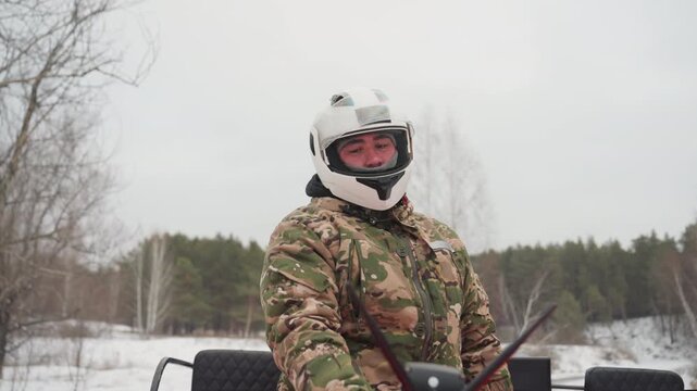 White man in camo helmet adjusting atv controls on snowy forest trail, checks mirror and engine, climbs onto red quad, readying for extreme offroad ride focused outdoorsman prepping gear, cold breath,