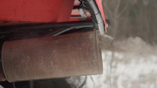 Rusted atv tailpipe blowing cold vapor underbody closeup showing muffler surface, visible exhaust plumes, snowdusted tires in background, engine revs creating smoky bursts, gritty metallic texture,