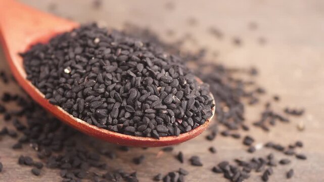 Close up shot of black cumin seeds in a wooden spoon, showcasing the rich texture and deep color of the spice, ideal for culinary and herbal themes.