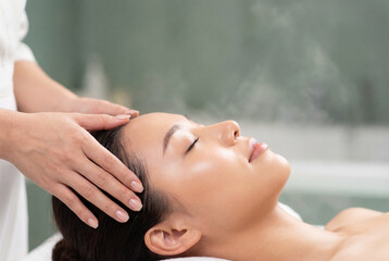Naklejka premium Relaxed asian woman enjoying a soothing head massage in a spa salon