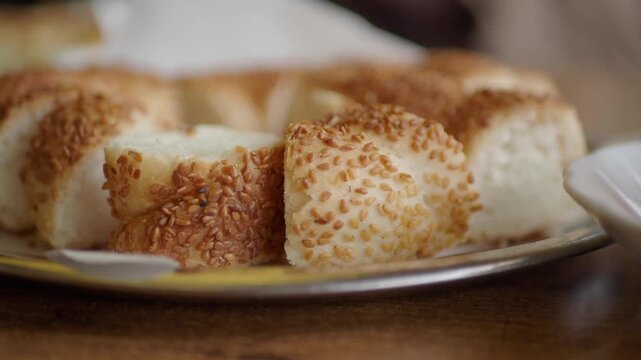 Close-up of sliced simit bread sprinkled with sesame seeds next to tea.