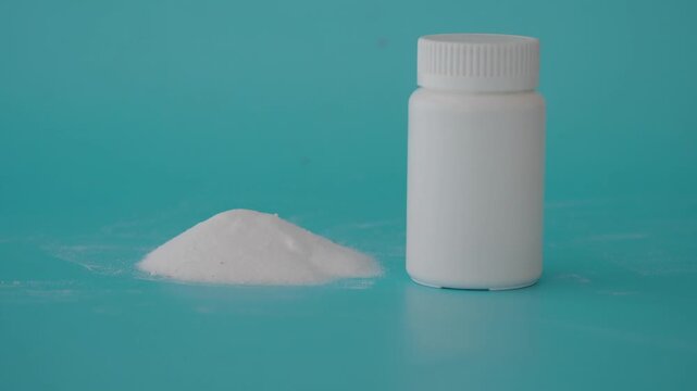 White plastic medicine bottle with pile of powder on blue background.