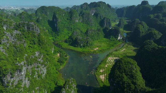 Scenic drone shot of Trang An UNESCO heritage site with winding river and dramatic karst formations.
