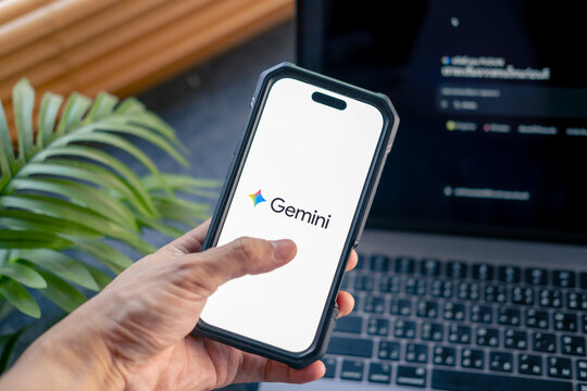 Phayao, Thailand - Mar 19 2026 : Gemini, Hand hold smartphone open on website on laptop display screen on the background.