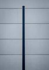 Fototapeta premium Vertical Steel Pipe Against Horizontal Panelled Building Facade Simplicity