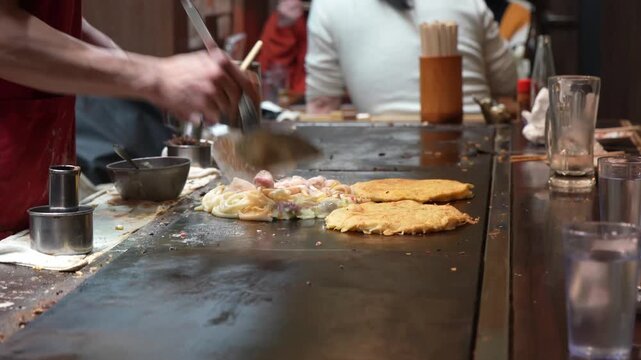Chef preparing okonomiyaki on teppan grill Japan