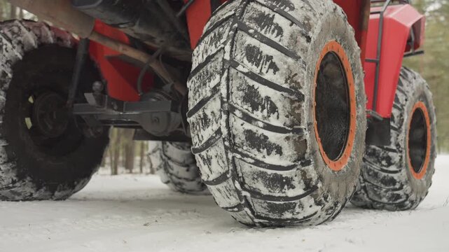 Closeup of icy atv tire with orange rim. Frozen mud and deep tread on snowy atv tire from low angle. Detailed macro shot of atv tire on snowcovered ground showing icy mud and bright orange rim