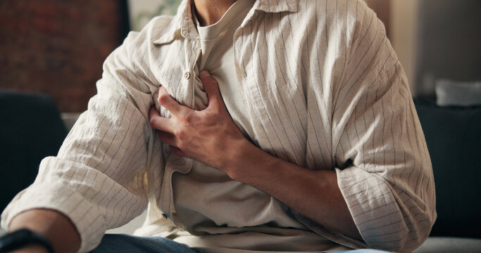 Man, hands and sick in home with chest pain, heart attack symptoms or discomfort for medical problem. Person, cardiac arrest and health issue in house with disease, illness and emergency in lounge.