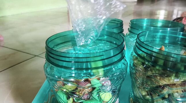 Colorful elephant ear crackers being poured from a plastic bag into a jar.