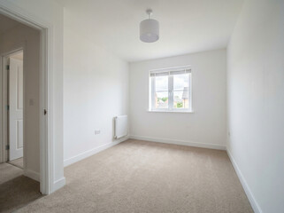 Obraz premium An empty room with white walls and a window showing a view of another house outside.