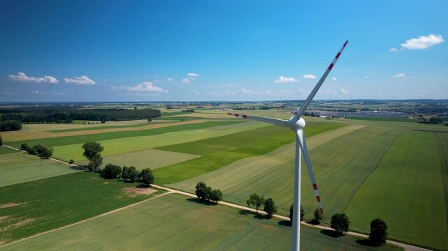 Aerial drone footage of a lone wind turbine spinning in green agricultural fields under a clear blue sky