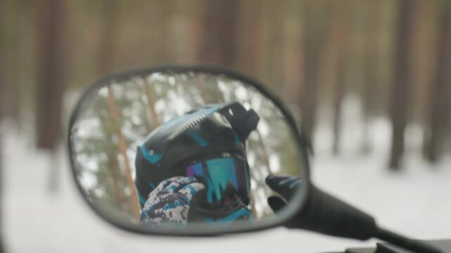 Snowy forest mirror closeup gearing up rider, helmet reflection shows focused glance and visor detail, gloved hand near throttle, subtle motion and blurred pines, tense adrenaline before extreme atv